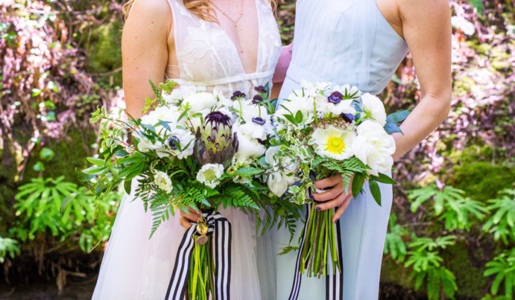 A Bride and Her Bridesmaid Posing for a Photo of their lush summer bouquets